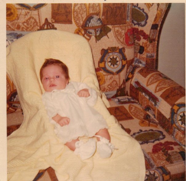 A picture of me at 3 months old laying on a 1970s style couch.